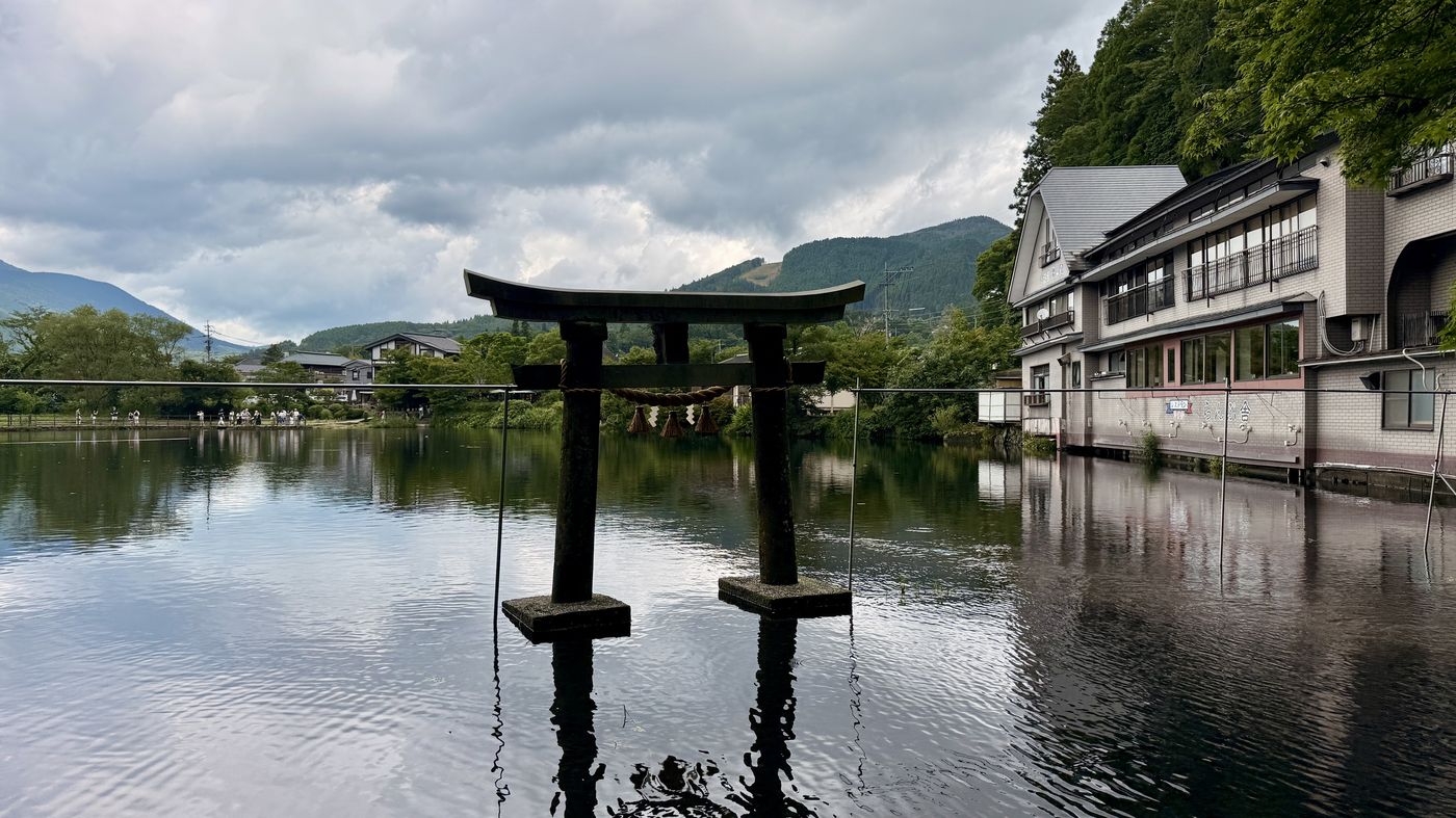 Stone torii gate standing in Lake Kinrin at Yufuin, with wooded mountains behind